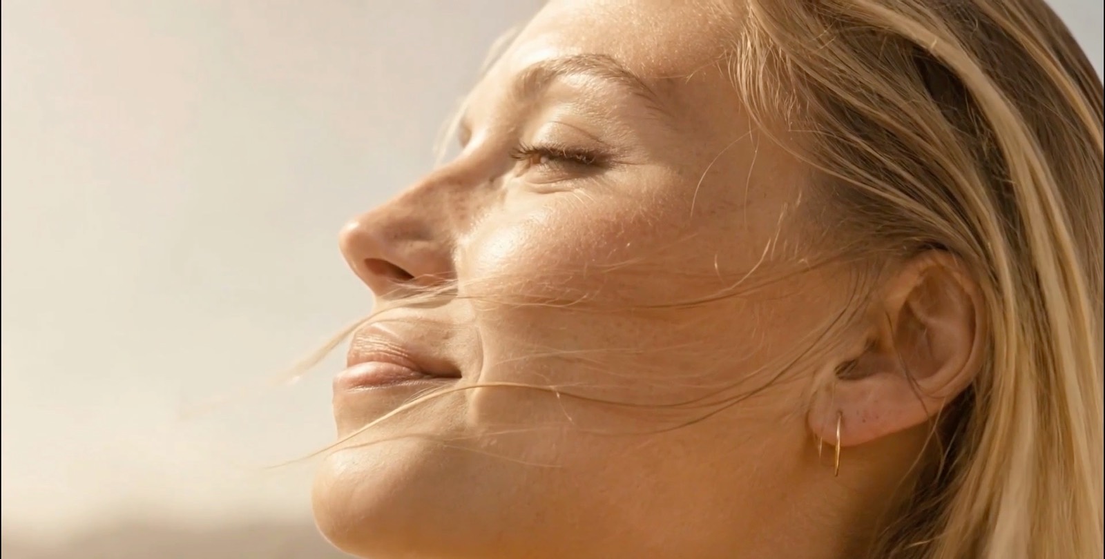 A woman with wind in her hair turns towards the light, calm and strong.